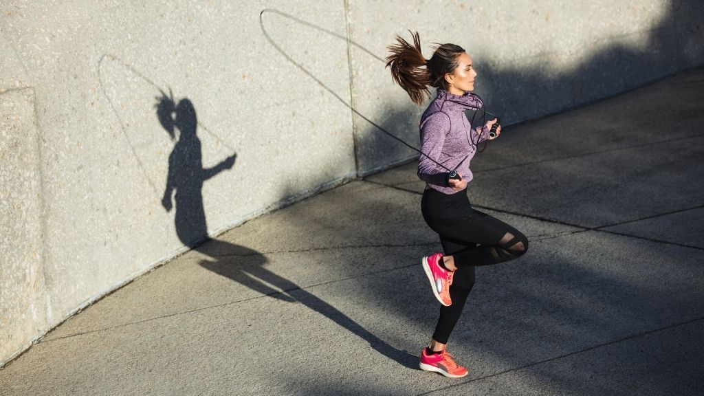 träningsklädd kvinna hoppar hopprep i solen mot bakrund i betong